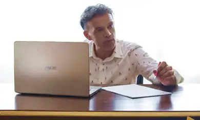 Tutor con camicia bianca parla davanti au un PC portatile